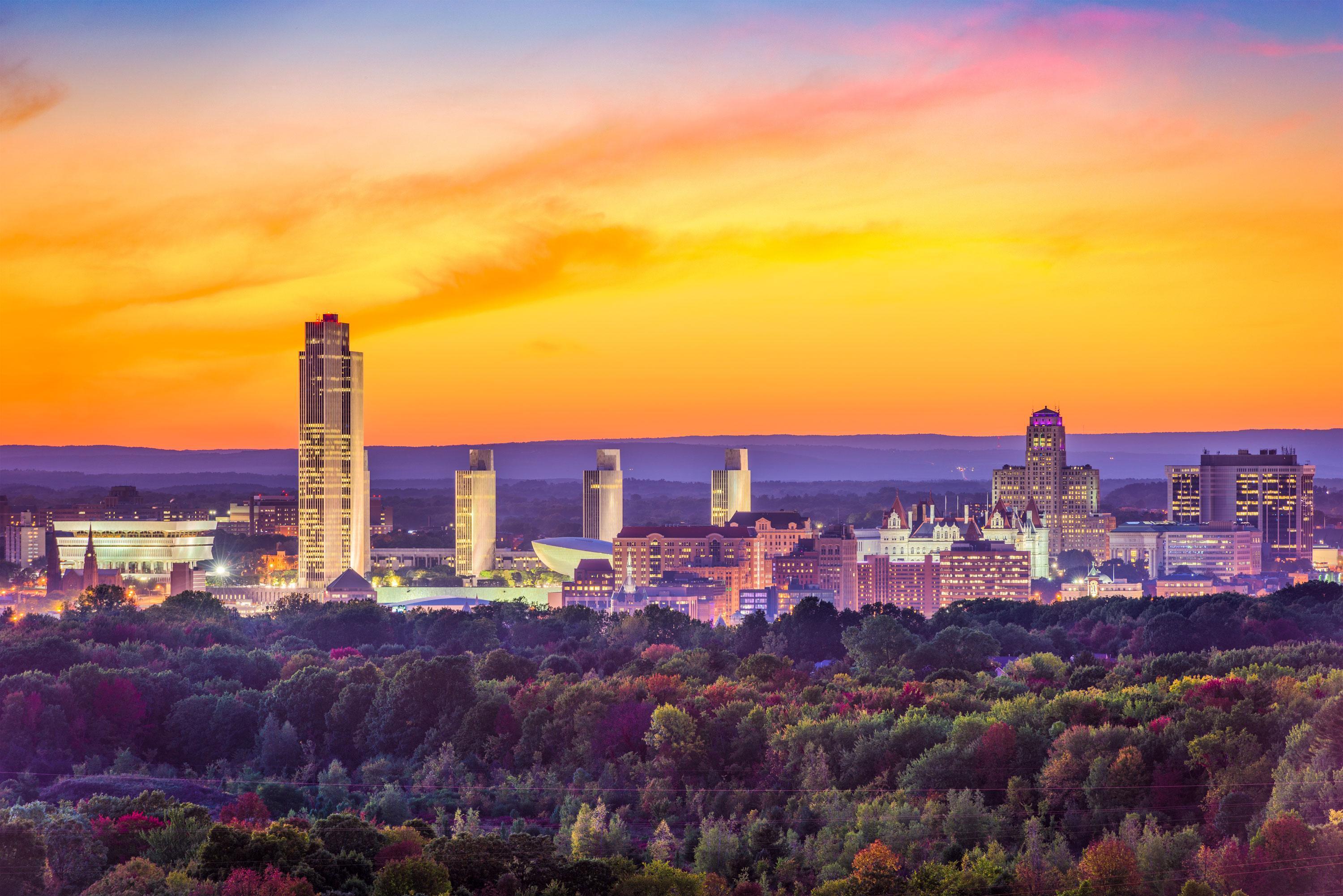 Albany, NY – Fall Season - Orange and yellow colored skyline hangs above the Albany deep blue and purple forest and buildings during a Sunset